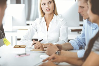 Bir grup iş adamı toplantıda soruları tartışıyor. Ofis görüşmelerinde iş arkadaşına gülümseyen sarışın iş kadınının vesikalığı. Şirket işgalinde takım çalışması ve işbirliği