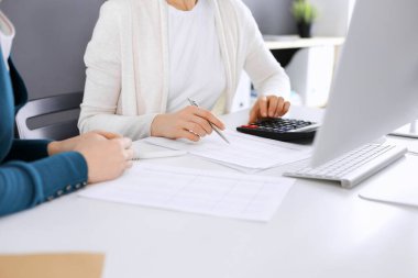 Muhasebeci mali durumu kontrol ediyor ya da vergi formları için hesap makinesi geliri ile sayıyor, eller yakın çekim. İş kadını ofisteki masada iş arkadaşıyla oturuyor ve çalışıyor. Denetim kavramı