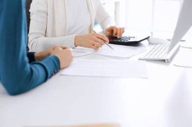 Muhasebeci mali durumu kontrol ediyor ya da vergi formları için hesap makinesi geliri ile sayıyor, eller yakın çekim. İş kadını ofisteki masada iş arkadaşıyla oturuyor ve çalışıyor. Denetim kavramı