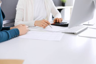 Muhasebeci mali durumu kontrol ediyor ya da vergi formları için hesap makinesi geliri ile sayıyor, eller yakın çekim. İş kadını ofisteki masada iş arkadaşıyla oturuyor ve çalışıyor. Denetim kavramı