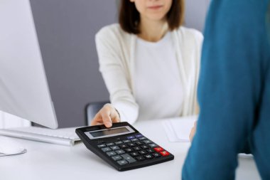 Muhasebeci mali durumu kontrol ediyor ya da vergi formları için hesap makinesi geliri ile sayıyor, eller yakın çekim. İş kadını ofisteki masada iş arkadaşıyla oturuyor ve çalışıyor. Denetim kavramı