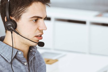 İnternette müşterilerle konuşurken kulaklık ve bilgisayar kullanan sıradan giyinmiş genç bir adam. Çağrı merkezi, iş konsepti
