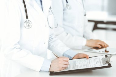 İş yerindeki bilinmeyen kadın doktorlar, arka planda hastaları var. Hastane resepsiyonunda beklerken tıbbi belgeleri dolduran kadın doktorlar, yakın plan. Sağlık hizmeti kavramı