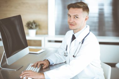 Klinikte ya da hastane ofisinde bilgisayar başında oturan bir doktor. Tıbbi vesikalık ve tıp konsepti