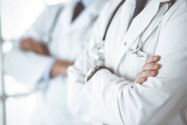 Hastane ofisinde kolları kavuşturulmuş bir ekip olarak bekleyen bir grup doktor, yakın plan. Tıbbi yardım, sağlık sigortası ve tıp konsepti