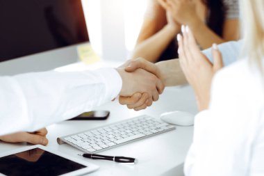 Güneşli ofiste el sıkışan iki işadamı, yakın plan. Meslektaşların başarıyı alkışlaması sona ermiştir.