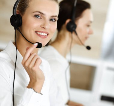 Sarışın kadın müşteri hizmetleri temsilcisi ve meslektaşı internetteki müşterilerine kulaklık kullanarak danışıyorlar. Çağrı merkezi ve iş adamları kavramı