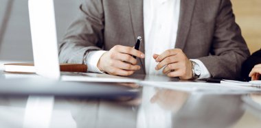 Bilinmeyen iş adamları ve kadınlar oturmuş, dizüstü bilgisayarlarını kullanıyorlar ve modern ofiste buluşmada soruları tartışıyorlar, yakın plan.