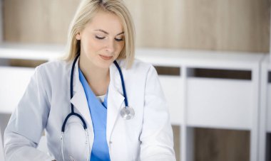 Hastanedeki ya da klinikteki masa başında oturan kadın doktor. Sarışın, neşeli doktor ilaç geçmişi formunu dolduruyor.