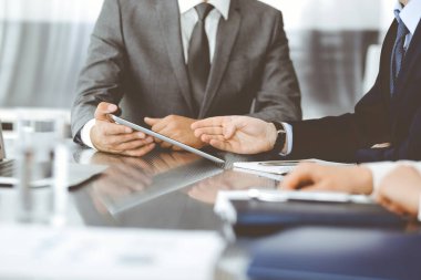 Bilinmeyen işadamı, modern ofisteki cam masada otururken tablet bilgisayar kullanıyor ve iş arkadaşıyla birlikte çalışıyor. Takım çalışması ve ortaklık kavramı