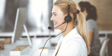 Sarışın iş kadını iletişim kurmak ve müşteri hizmetlerindeki insanlara danışmak için kulaklık kullanıyor. Merkezi ara. Bir grup operatör iş başında