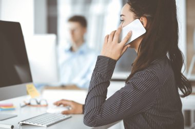 Modern ofisteki işyerinde bilgisayar kullanan bir iş kadını. Esmer sekreter ya da kadın avukat gülümsüyor ve mutlu görünüyor. Zevk ve başarı için çalışmak