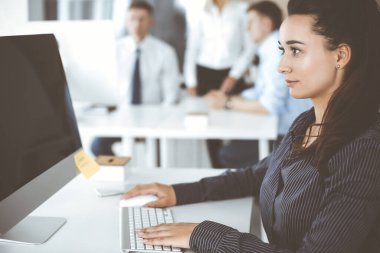 Modern ofisteki işyerinde bilgisayar kullanan bir iş kadını. Esmer sekreter ya da kadın avukat kameraya bakıyor ve mutlu gülümsüyor. Zevk ve başarı için çalışmak