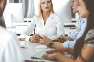 Bir grup iş adamı toplantıda soruları tartışıyor. Ofis görüşmelerinde iş arkadaşına gülümseyen sarışın iş kadınının vesikalığı. Şirket işgalinde takım çalışması ve işbirliği