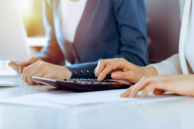 Mali durumu kontrol eden ya da vergi formları için hesap makinesinin geliri ile sayan, elleri yakın çekim. İş kadını ofisteki masada iş arkadaşıyla oturuyor ve çalışıyor. Vergi ve Denetim kavramı