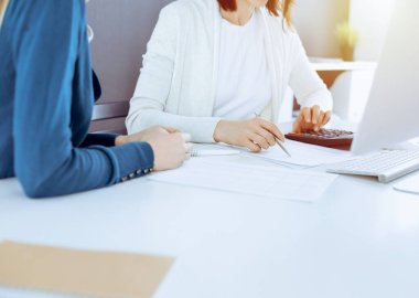 Mali durumu kontrol eden ya da vergi formları için hesap makinesinin geliri ile sayan, elleri yakın çekim. İş kadını ofisteki masada iş arkadaşıyla oturuyor ve çalışıyor. Vergi ve Denetim kavramı