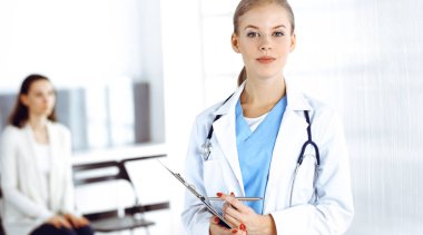 Kadın - doktor hastanın arka planında klinikte tıbbi geçmiş kayıtlarını doldurmak için pano kullanıyor. Tıp konsepti