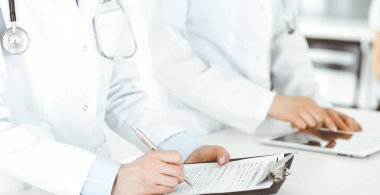 Arka planda hastası olan iki kadın doktor var. Resepsiyonda tıbbi belgeleri dolduran kadın doktorlar, yakın çekim. Tıptaki veriler