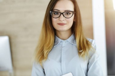 Güneşli ofiste iş kadını vesikalığı. Bilinmeyen iş kadını tablet bilgisayarla ayakta duruyor. Genç muhasebeci ya da sekreter iyi görünüyor.