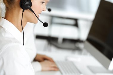 Sarışın kadın müşteri hizmetleri temsilcisi ve meslektaşı internetteki müşterilerine kulaklık kullanarak danışıyorlar. Çağrı merkezi ve iş adamları kavramı