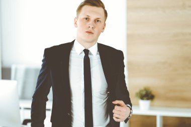 Ofisteki kameraya bakıp duran neşeli iş adamı. Genç ve başarılı girişimcinin vesikalığı