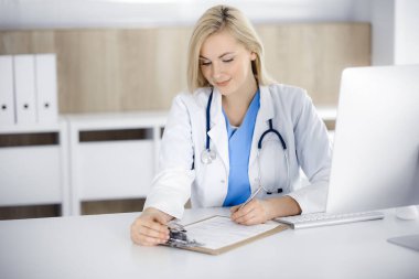 Hastanedeki ya da klinikteki masa başında oturan kadın doktor. Sarışın, neşeli doktor ilaç geçmişi formunu dolduruyor.