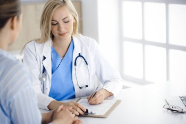 Kadın doktor ve hasta hastanede ya da klinikte oturup konuşuyorlar. Sarışın terapist neşeyle gülümsüyor. Tıp konsepti