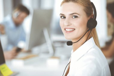 Sarışın iş kadını iletişim kurmak ve müşteri hizmetlerindeki insanlara danışmak için kulaklık kullanıyor. Merkezi ara. Bir grup operatör iş başında