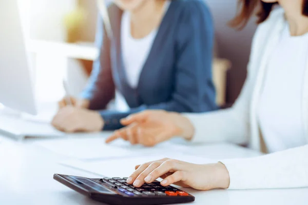 Accountant checking financial statement or counting by calculator income for tax form, hands closeup. Business woman sitting and working with colleague at the desk in office. Tax and Audit concept