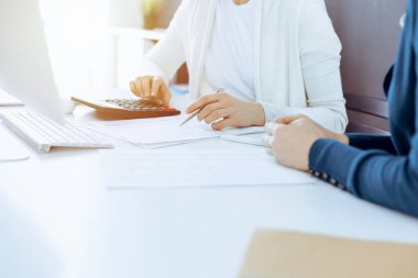 Mali durumu kontrol eden ya da vergi formları için hesap makinesinin geliri ile sayan, elleri yakın çekim. İş kadını ofisteki masada iş arkadaşıyla oturuyor ve çalışıyor. Vergi ve Denetim kavramı