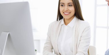 Masasında oturan genç bir kadın, beyaz renkli bir ofiste bilgisayarla. Görünüşe göre öğrenci kız ya da iş kadını sıradan giyinmiş bir adamla iletişim kuruyor.