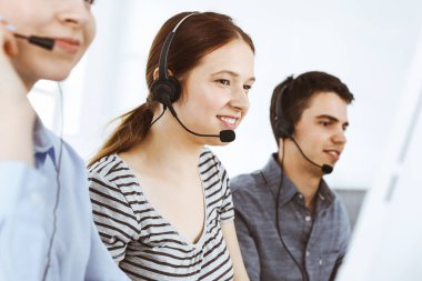 İnternette müşterilerle konuşurken kulaklık ve bilgisayar kullanan sıradan giyinmiş genç bir kadın. Bir grup operatör iş başında. Çağrı merkezi, iş konsepti