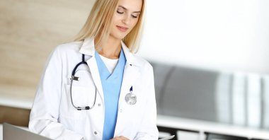 Klinikteki kadın doktor mesleğinden dolayı heyecanlı ve mutlu. Sarışın kadın doktor tablet bilgisayar kullanırken gülümsüyor. Tıp konsepti