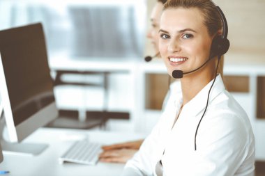 Sarışın kadın müşteri hizmetleri temsilcisi ve meslektaşı internetteki müşterilerine kulaklık kullanarak danışıyorlar. Çağrı merkezi ve iş adamları kavramı