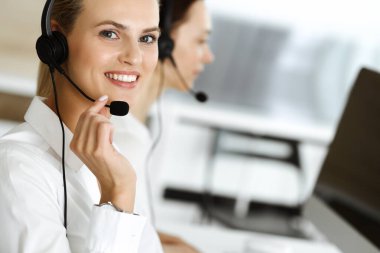 Sarışın kadın müşteri hizmetleri temsilcisi ve meslektaşı internetteki müşterilerine kulaklık kullanarak danışıyorlar. Çağrı merkezi ve iş adamları kavramı