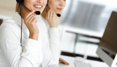 Sarışın kadın müşteri hizmetleri temsilcisi ve meslektaşı internetteki müşterilerine kulaklık kullanarak danışıyorlar. Çağrı merkezi ve iş adamları kavramı