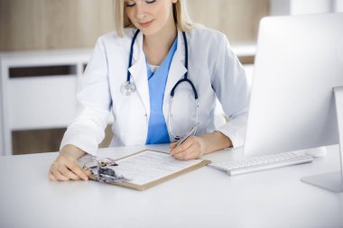 Hastanedeki ya da klinikteki masa başında oturan kadın doktor. Sarışın, neşeli doktor ilaç geçmişi formunu dolduruyor.