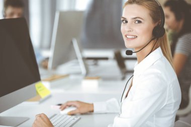 Sarışın iş kadını iletişim kurmak ve müşteri hizmetlerindeki insanlara danışmak için kulaklık kullanıyor. Merkezi ara. Bir grup operatör iş başında