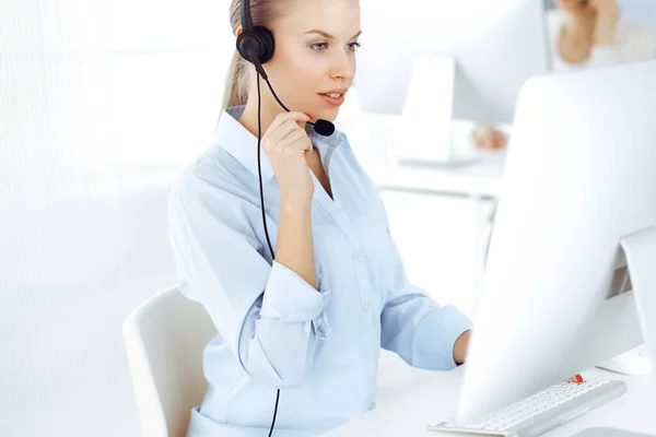 A szőke nő híváskezelő számítógépet és fejhallgatót használ, hogy online konzultáljon az ügyfelekkel. Különböző emberek csoportja, akik ügyfélszolgálati foglalkozásként dolgoznak. Üzleti koncepció — Stock Fotó