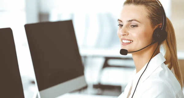 Blond female customer service representative is consulting clients online using headset. Call center and business concept