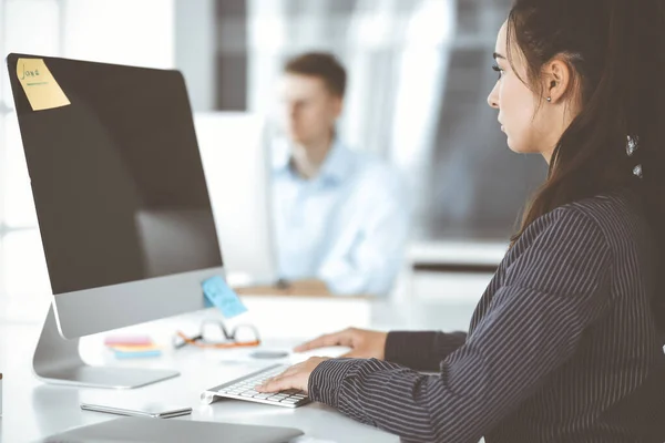 Business woman using computer at workplace in modern office. Brunette secretary or female lawyer smiling and looks happy. Working for pleasure and success