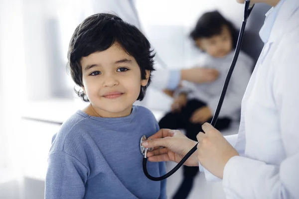 Orvos-nő sztetoszkóppal vizsgál meg egy gyermekbeteget. Aranyos arab fiú és a bátyja az orvosi vizsgálaton. Orvosi fogalom — Stock Fotó