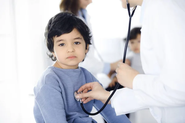 Médico-mujer examinando a un niño paciente por estetoscopio. Lindo chico árabe y su hermano en la cita con el médico. Concepto de medicina —  Fotos de Stock