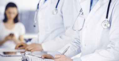 İş yerindeki bilinmeyen kadın doktorlar, arka planda hastaları var. Hastane resepsiyonunda beklerken tıbbi belgeleri dolduran kadın doktorlar, yakın plan. Sağlık hizmeti kavramı