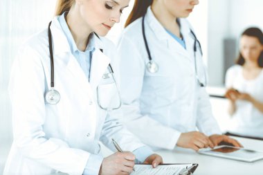 İşteki iki kadın doktor ve hasta arka planda. Hastane resepsiyonunda beklerken tıbbi belgeleri dolduran kadın doktorlar. Tıptaki veriler