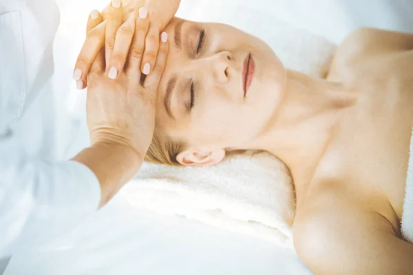 Mujer feliz disfrutando de masaje facial con los ojos cerrados en el salón de spa. Tratamiento relajante en medicina y concepto de belleza —  Fotos de Stock