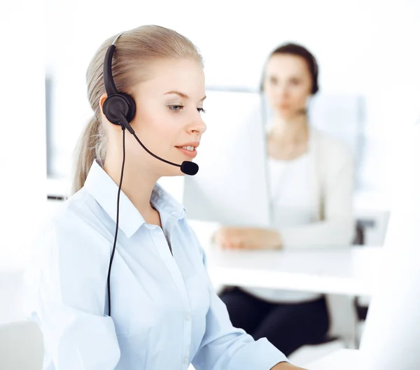 ブロンドの女性コールオペレーターは、オンラインでクライアントに相談するためにコンピュータとヘッドセットを使用しています。顧客サービスの職業として働く多様な人々のグループ。事業概念 — ストック写真
