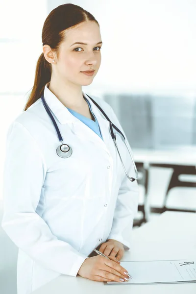 Γυναίκα-γιατρός στη δουλειά. Γυναίκα γιατρός ή εσωτερική φοιτητής συμπληρώνοντας ιατρικά έγγραφα ή συνταγή, ενώ στέκεται στην υποδοχή κλινική. Δεδομένα στην ιατρική — Φωτογραφία Αρχείου