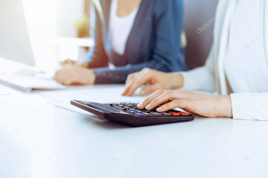 Accountant checking financial statement or counting by calculator income for tax form, hands closeup. Business woman sitting and working with colleague at the desk in office. Tax and Audit concept