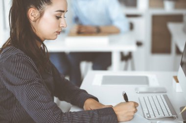 Modern ofisteki işyerinde bilgisayar kullanan bir iş kadını. Esmer sekreter ya da kadın avukat kameraya bakıyor ve mutlu gülümsüyor. Zevk ve başarı için çalışmak